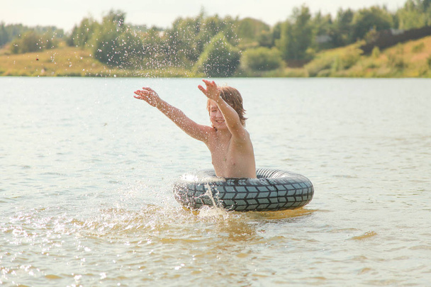 Милый мальчик веселится, играя с надувным плавательным кольцом в жаркий летний день
. - Фото, изображение