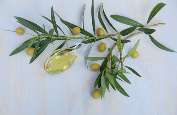 Flat lay organic olive oil in a glass in the form of olives and olive branch with olives on a blue wooden background. Ingredients for the kitchen. Healthy eating Mediterranean diet. With copy space for text, banner, pattern. - 写真・画像