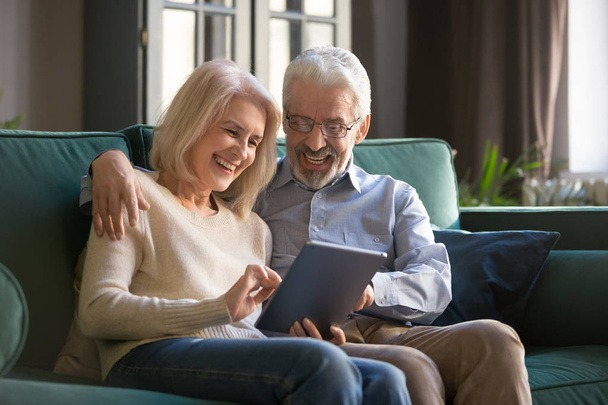 Heureux vieux couple assis sur le canapé en utilisant une tablette numérique
 - Photo, image