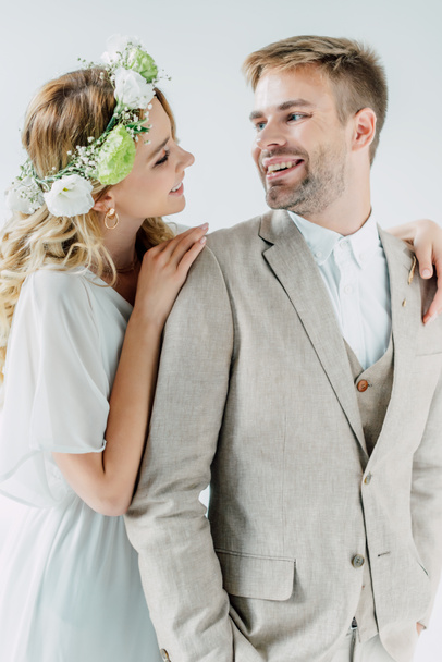 attraktive Braut und schöner Bräutigam lächeln und schauen einander vereinzelt auf grau an - Foto, Bild