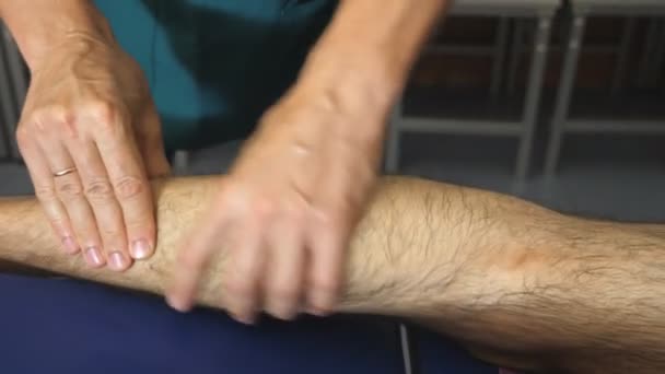 Mannelijke handen van professionele masseur Healing masseren voet van jonge sportman met olie in de melkstal. Armen van massagist doen langzaam massage been van atleet liggend op massagetafel in salon. Close-up - Video