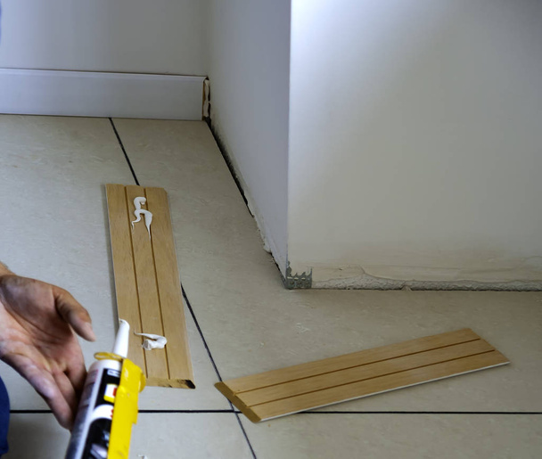 работник наносит клей на деревянную плинтус для крепления на стену
 - Фото, изображение