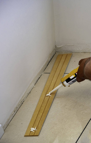 trabajador aplica pegamento en zócalo de madera para montaje en pared
 - Foto, Imagen