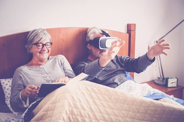 yaşlı çift gözlük kulaklık kullanarak adam yatakta oturuyor  - Fotoğraf, Görsel