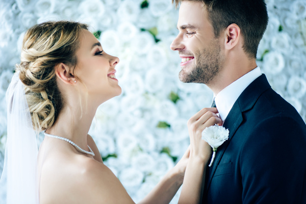 attractive bride and handsome bridegroom smiling and looking at each other  - Fotografie, Obrázek