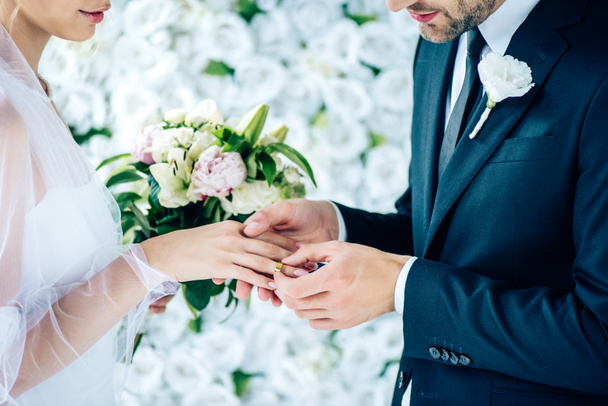 abgeschnittene Ansicht des Bräutigams, der Ehering an Finger legt  - Foto, Bild