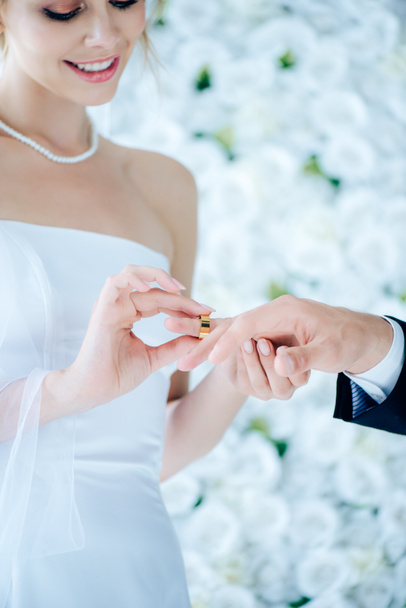 attractive and smiling bride putting wedding ring on finger  - Fotografie, Obrázek