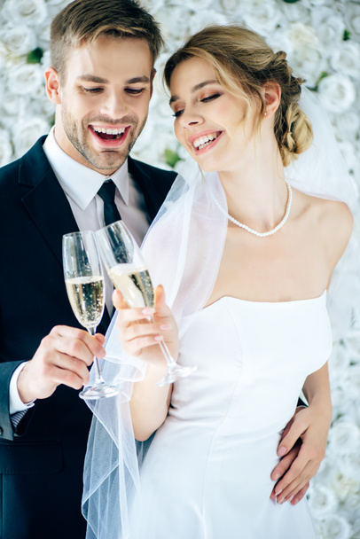 attractive bride and handsome bridegroom smiling and clinking with champagne glasses - Foto, Imagen
