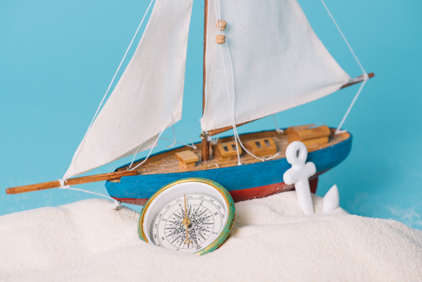 close up view of decorative ship near anchor and compass in white sand isolated on blue - Photo, Image