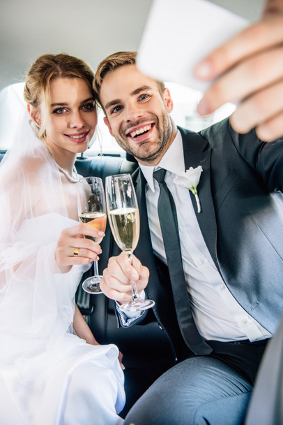 attraktive Braut und schöner Bräutigam machen Selfie im Auto  - Foto, Bild