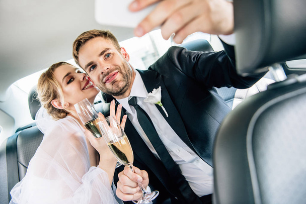 attractive bride and handsome bridegroom taking selfie in car  - Foto, imagen