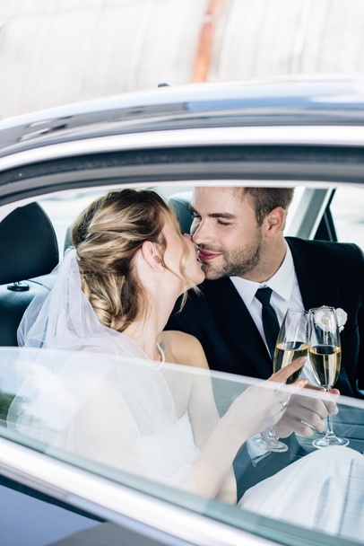attractive bride and handsome bridegroom kissing and clinking with champagne glasses - Foto, immagini