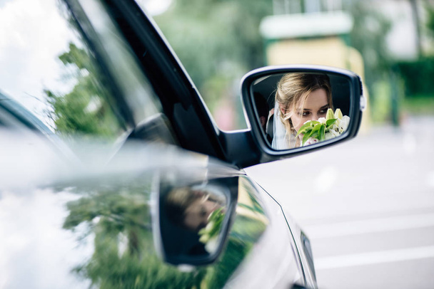 reflection of attractive and blonde bride smelling bouquet in car  - Valokuva, kuva