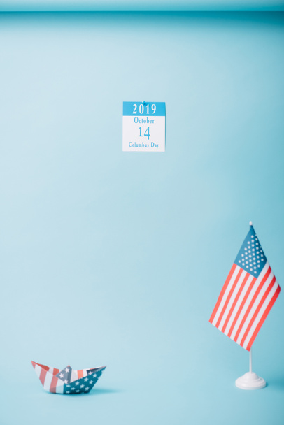 calendario de papel con inscripción Día de Colón cerca de barco de papel y bandera nacional estadounidense sobre fondo azul
 - Foto, imagen