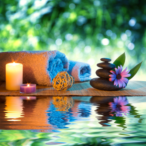 twee kaarsen en handdoeken zwarte stenen en paarse daisy op water - Foto, afbeelding
