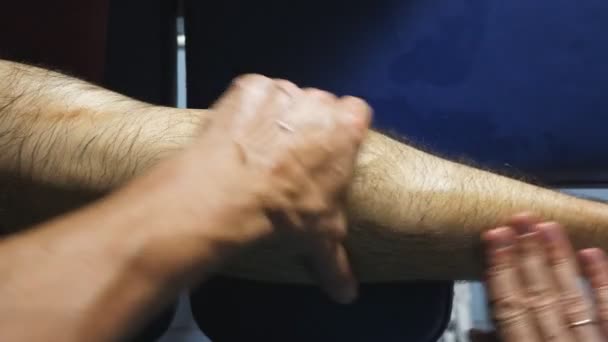Mężczyzna ręce massagist robi powoli masaż stóp młodego sportowca w salonie. Ramiona profesjonalnego masażysty uzdrowienie masażu nogi sportowca leżącego na stole do masażu w salonie. POV zwolnionym tempie - Materiał filmowy, wideo