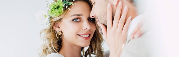 panoramic shot of attractive bride and handsome bridegroom hugging and looking at camera isolated on white  - Foto, imagen