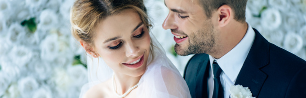 panoramatický záběr atraktivní nevěsty a pohledného ženicha, který se usmívá a dívá se na sebe  - Fotografie, Obrázek