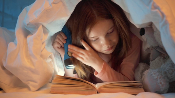 scared kid under blanket reading book with flashlight at night - Footage, Video
