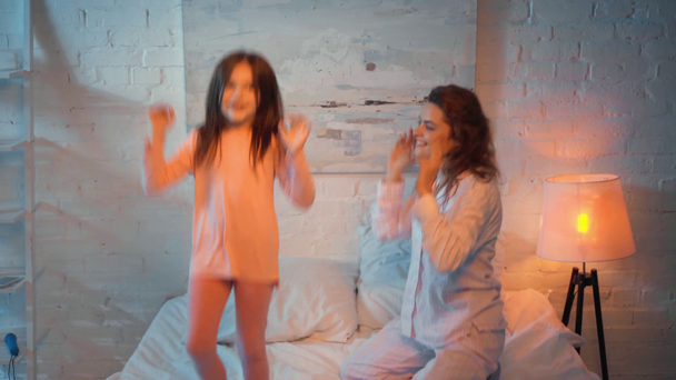 mother and daughter jumping on bed at night - Filmati, video