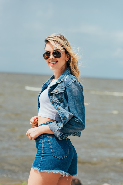 attractive woman in denim jacket and shorts looking at camera  - Фото, зображення