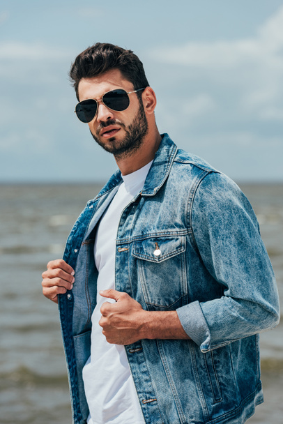 handsome man in denim jacket and sunglasses looking at camera  - Foto, immagini