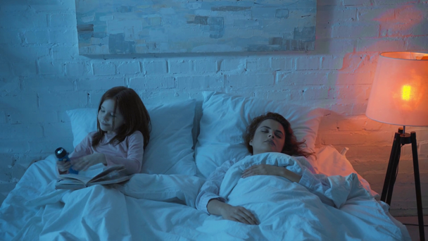 madre durmiendo e hija leyendo libro con linterna
 - Metraje, vídeo