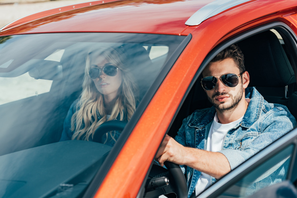 ελκυστική γυναίκα και όμορφος άντρας σε σακάκια denim κάθονται στο αυτοκίνητο - Φωτογραφία, εικόνα
