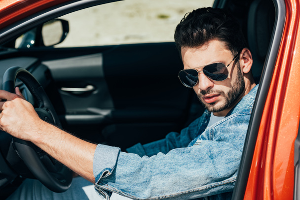 handsome man in sunglasses and denim jacket sitting in car - Foto, afbeelding