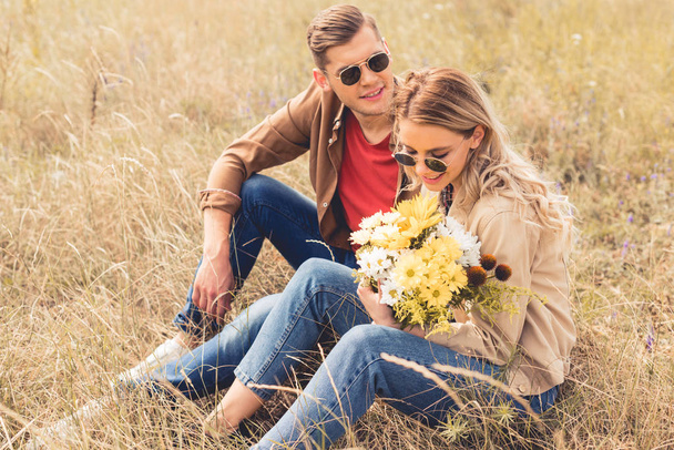 attractive woman with bouquet and handsome man smiling and sitting outside  - Foto, imagen
