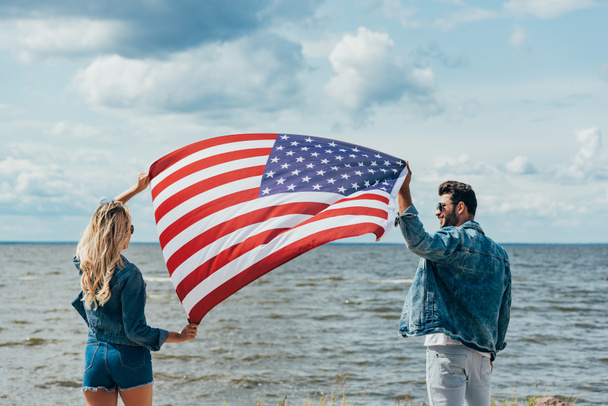 blonde woman and man in jacket holding american flag  - Φωτογραφία, εικόνα