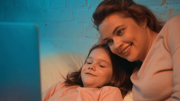 ευτυχισμένη μητέρα και κόρη χρησιμοποιώντας το laptop στο κρεβάτι τη νύχτα - Πλάνα, βίντεο