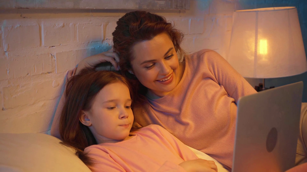 anne ve kızı gece yatakta dizüstü bilgisayarda film izlerken - Video, Çekim