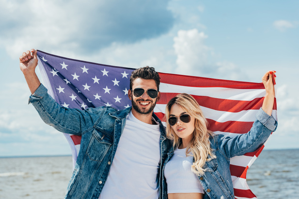 attraktive Frau und schöner Mann lächelnd und mit amerikanischer Flagge  - Foto, Bild