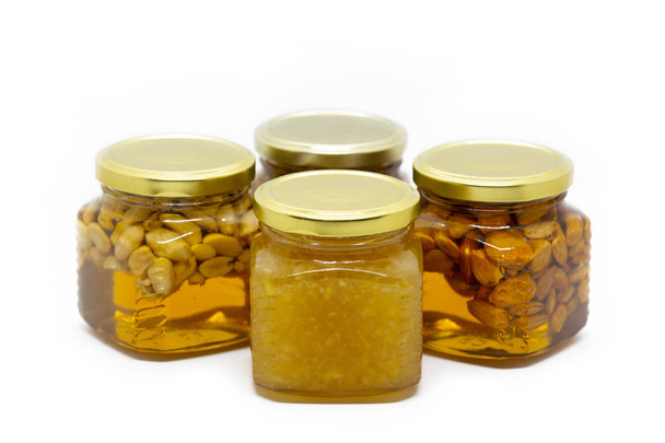 Piramide van glazen potten met honing met noten en citroen op witte achtergrond - Foto, afbeelding