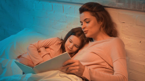 mother and daughter lying in bed and reading book together - Footage, Video