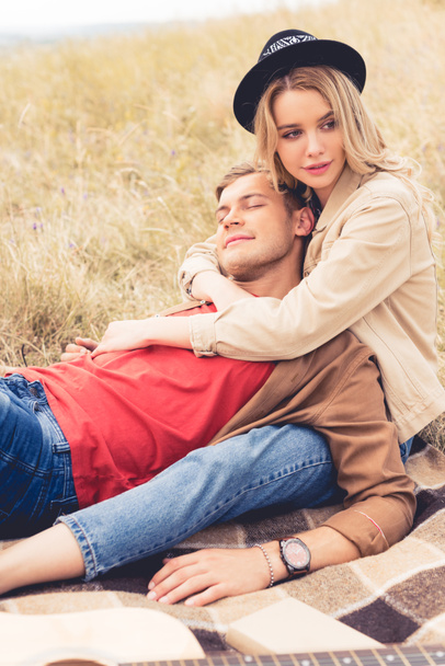 handsome man and attractive woman hugging and sitting on blanket  - Φωτογραφία, εικόνα