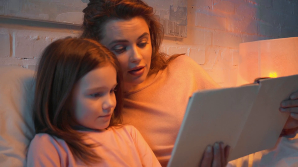mother and daughter reading book together in bed at night - Footage, Video