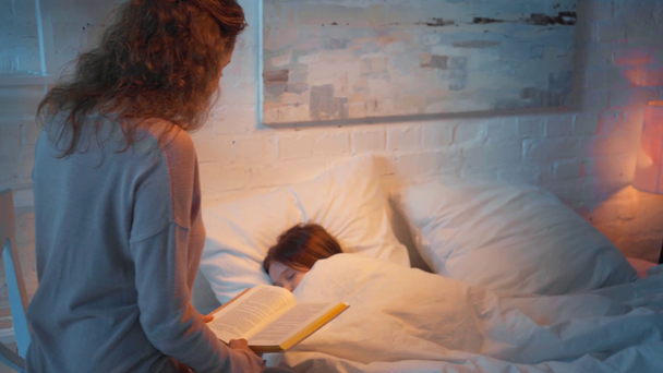 Maminka čte knihu, zatímco dcera spí v noci v posteli - Záběry, video