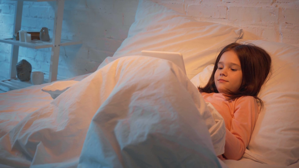 emotional child using digital tablet in bed at night - Záběry, video