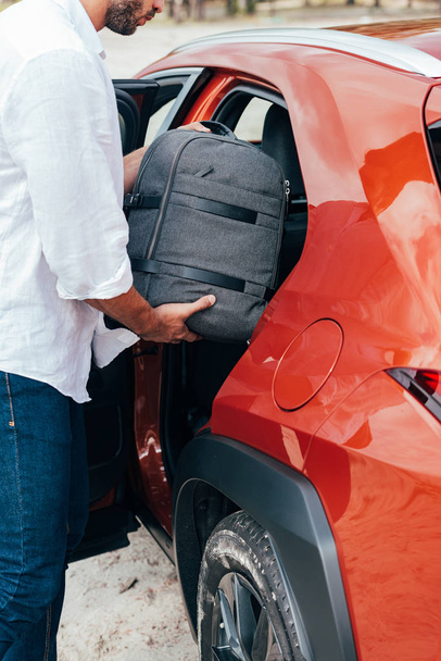 cropped view of man in shirt putting backpack in car  - Foto, Imagem