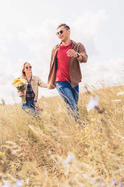 attractive woman and handsome man in sunglasses walking and holding hands  - Fotografie, Obrázek