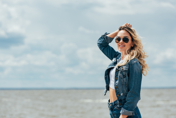 blonde and attractive woman in denim jacket and sunglasses looking away  - Фото, зображення