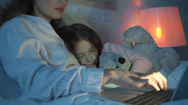 madre usando laptop mientras hija durmiendo con osito de peluche
 - Metraje, vídeo