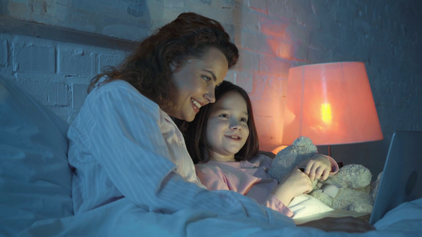 счастливые мать и дочь с плюшевым мишкой смотреть фильм в постели
 - Кадры, видео