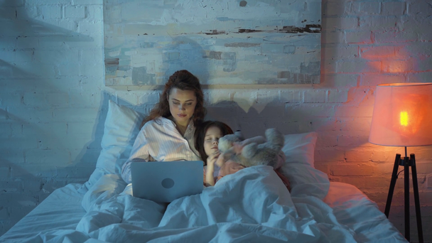 Mutter benutzt Laptop, während Tochter nachts mit Teddybär schläft - Filmmaterial, Video