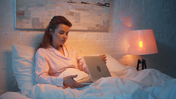 dorosły kobieta ziewanie podczas korzystania z laptopa w łóżku w nocy - Materiał filmowy, wideo