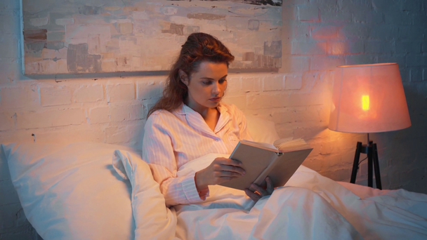 aikuinen nainen lukee kirjaa sängyssä yöllä
 - Materiaali, video