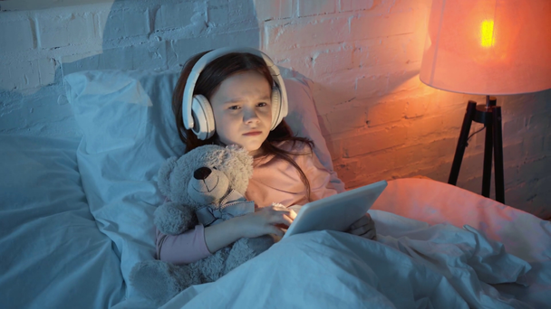 niño escuchando música en auriculares, bailando y usando tableta digital en la cama
 - Metraje, vídeo