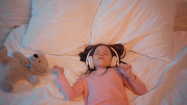 lapsi kuuntelee musiikkia kuulokkeet kun makaa sängyssä
 - Materiaali, video